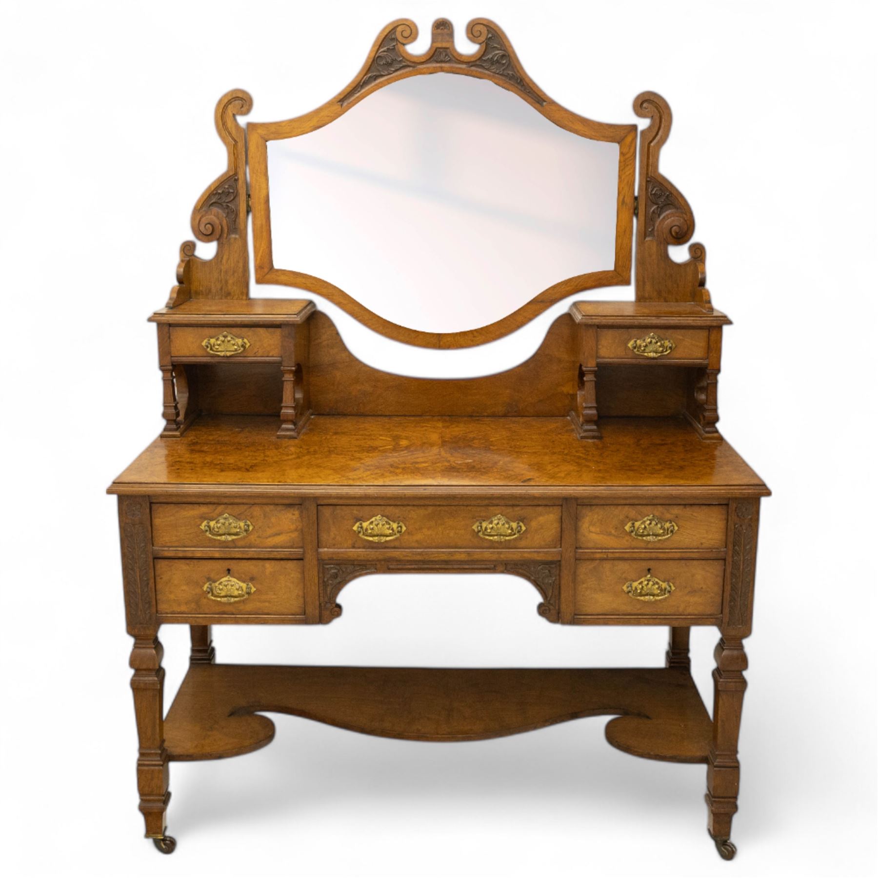Late Victorian burr walnut veneer dressing table, the arched swing mirror surmounted by pierced scroll cresting, flanked by twin drawers on turned columns, over moulded rectangular top with five drawer arrangement, on block supports with shaped undertier