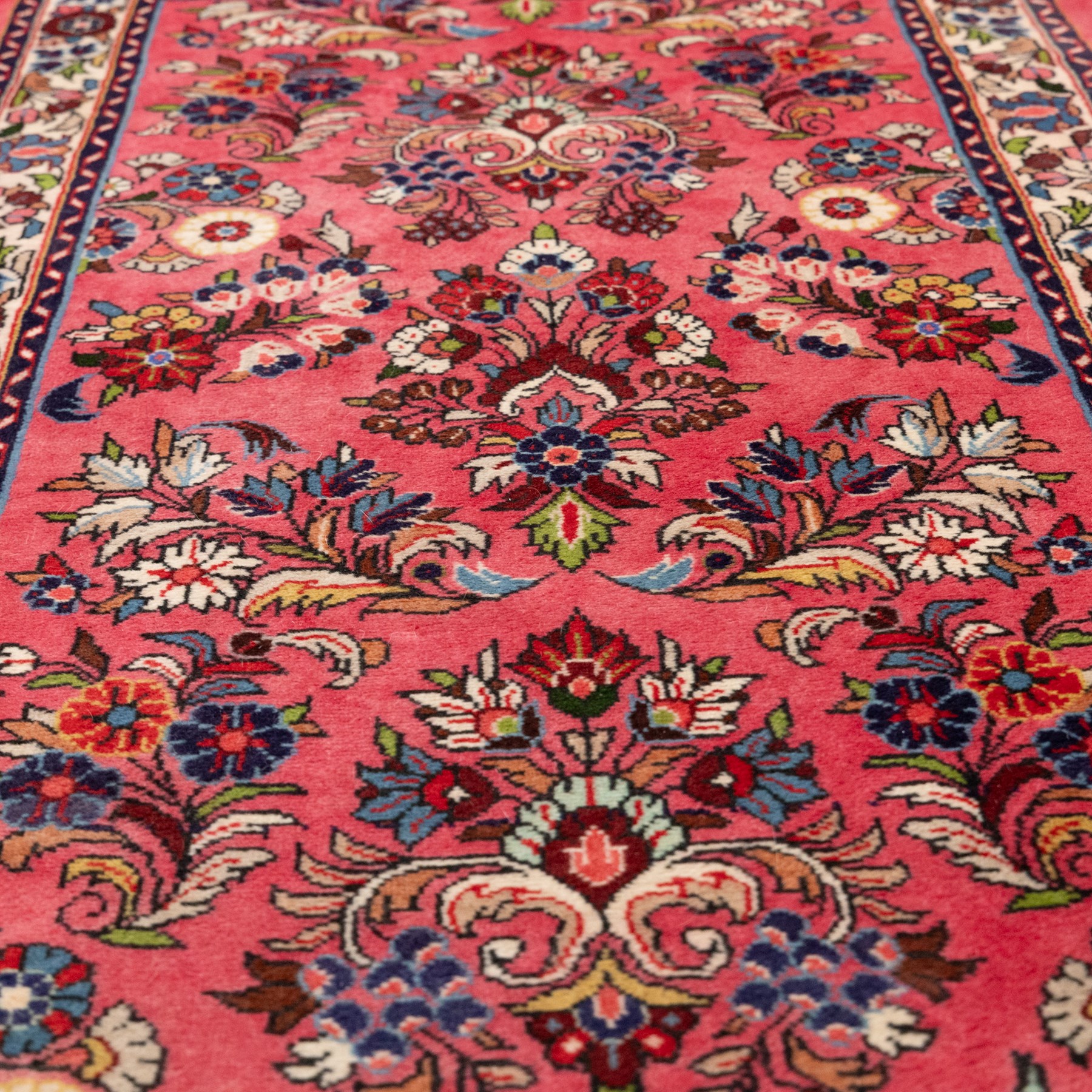Persian rose ground runner rug, the field decorated with repeating polychrome floral sprays and scrolling palmettes, enclosed by an ivory floral border and narrow navy geometric guard stripes