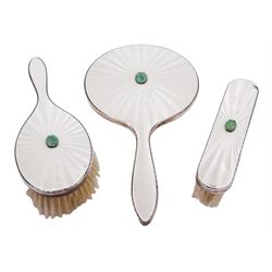 Mid 20th century silver mounted three piece dressing table set, comprising hand mirror, hair brush and clothes brush, each with white guilloche enamel decoration and set with a carved green hardstone, hallmarked Henry Clifford Davis, Birmingham 1959