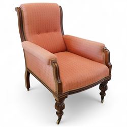 Victorian mahogany framed armchair, upholstered in salmon pink dot patterned fabric, the moulded arms with carved scroll terminals, raised on turned and fluted front legs and swept back legs, all with castors