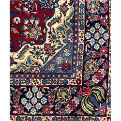 Central Persian Isfahan Carpet, hand-knotted, featuring a bold central rosette medallion on a rich red field, flanked by stylised floral sprays, scrolling foliage and mythical animals, within a broad indigo border decorated with alternating cartouches and flowerheads