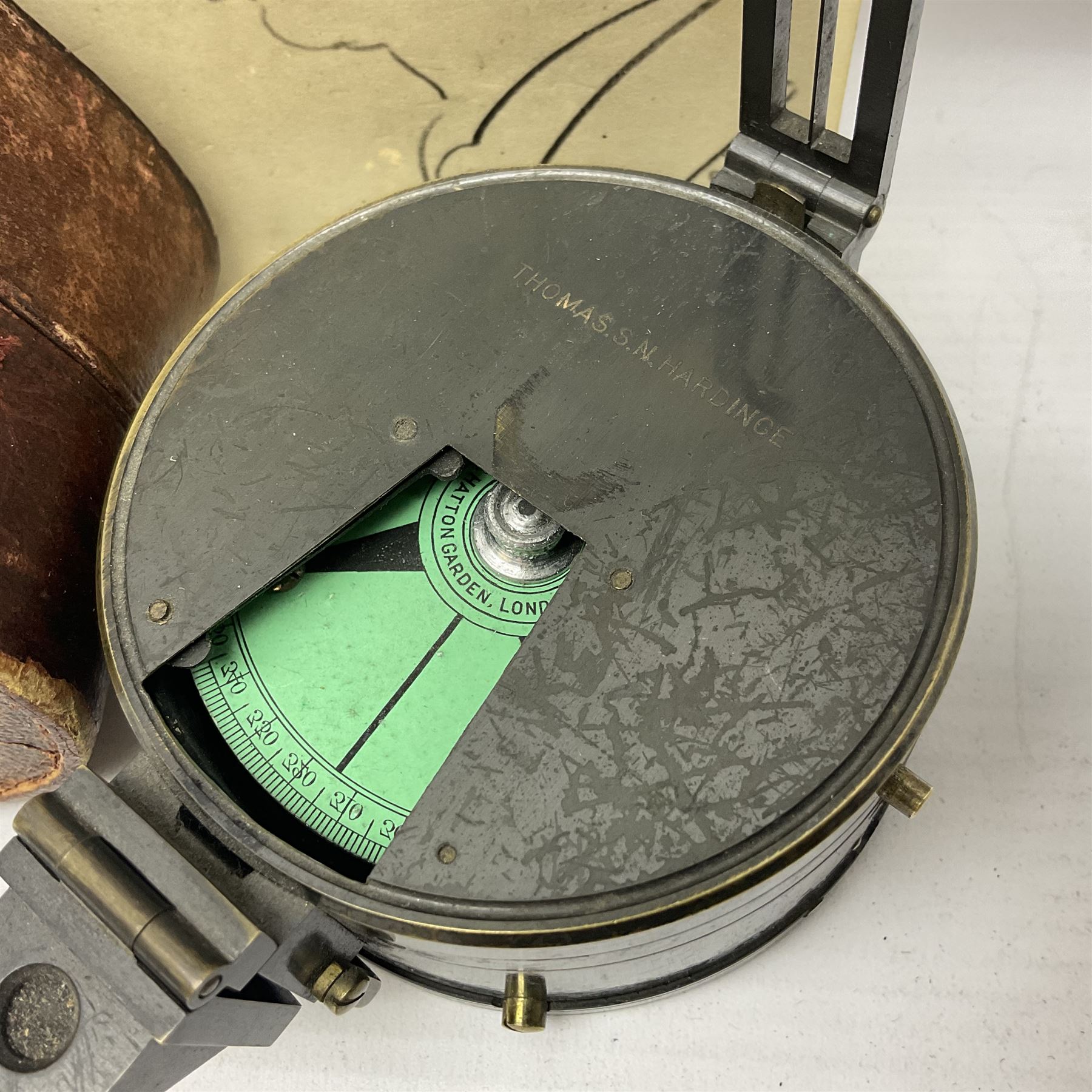 19th century Watkins combined clinometer and compass, patent 217, by J. Hicks Maker 8 Hatton Garden London No.5829, of drum shaped form in lacquered brass case D7cm; both instrument and case bear the name of former owner Thomas S.N. Hardinge; with early 20th century postcard caricature of a serviceman (2)