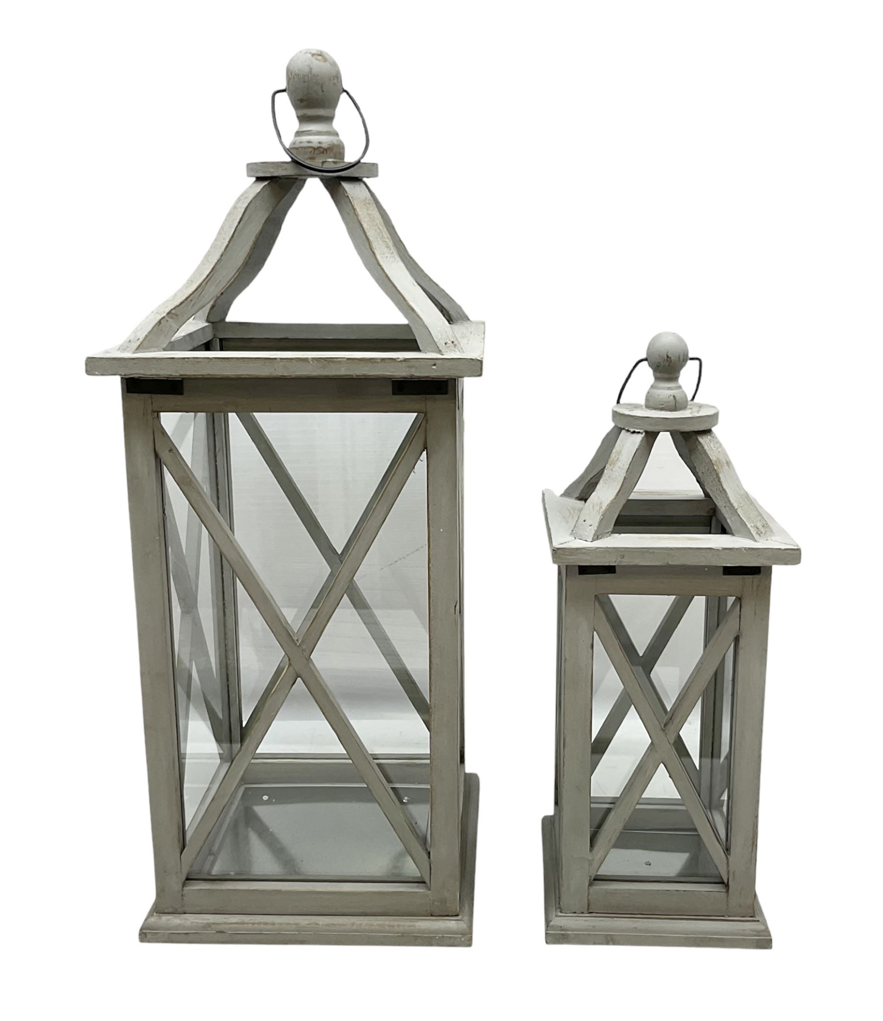 Two wooden lanterns with four glass sides, loop handles and open tops, largest example 58cm