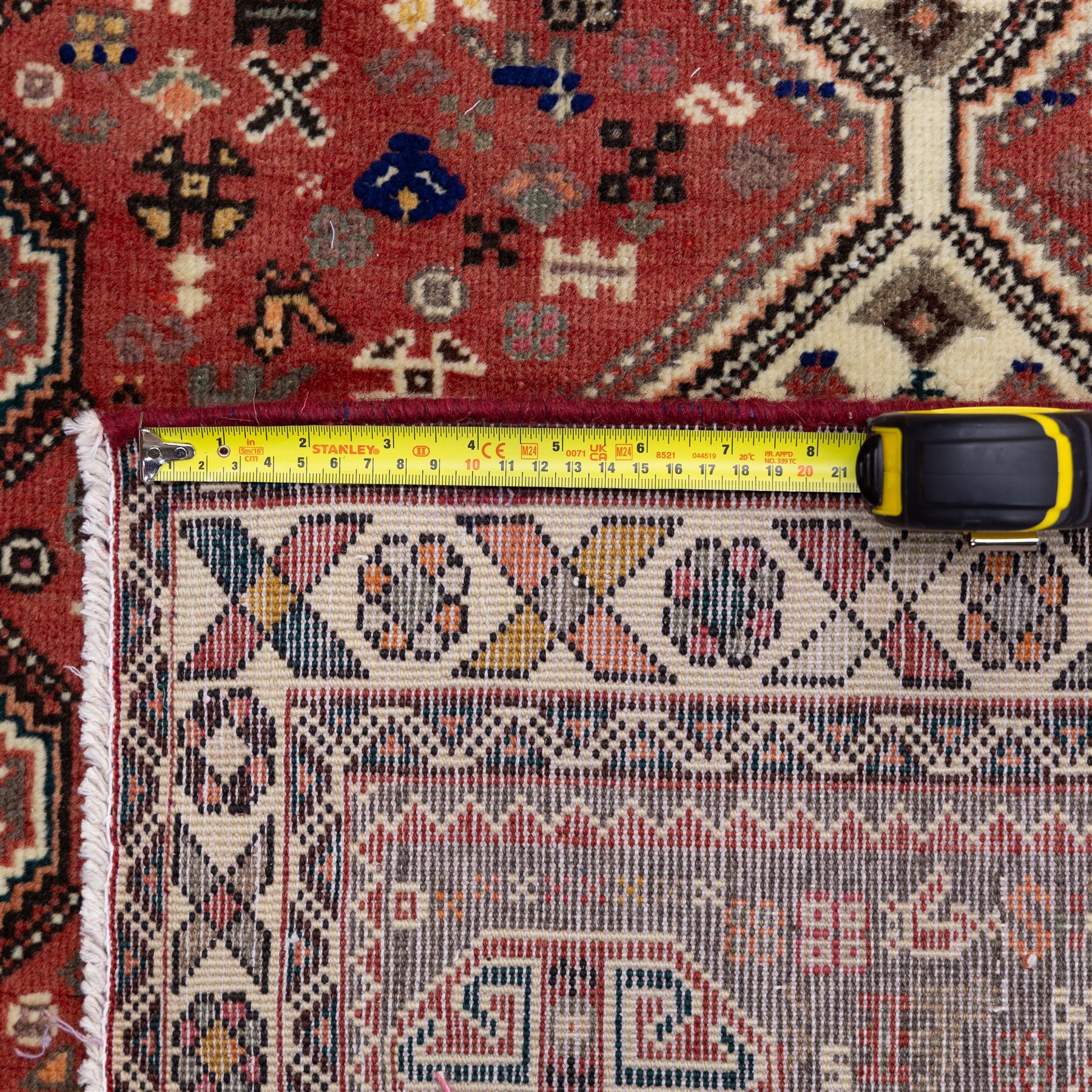South West Persian Abadeh hand-knotted runner, madder red field decorated with a vertical sequence of stepped lozenge medallions, each enclosing stylized geometric motifs and angular devices, surrounding field filled with tribal symbols and abstract forms, enclosed within a narrow main border and flanked by multiple guard stripes, with fringe ends 