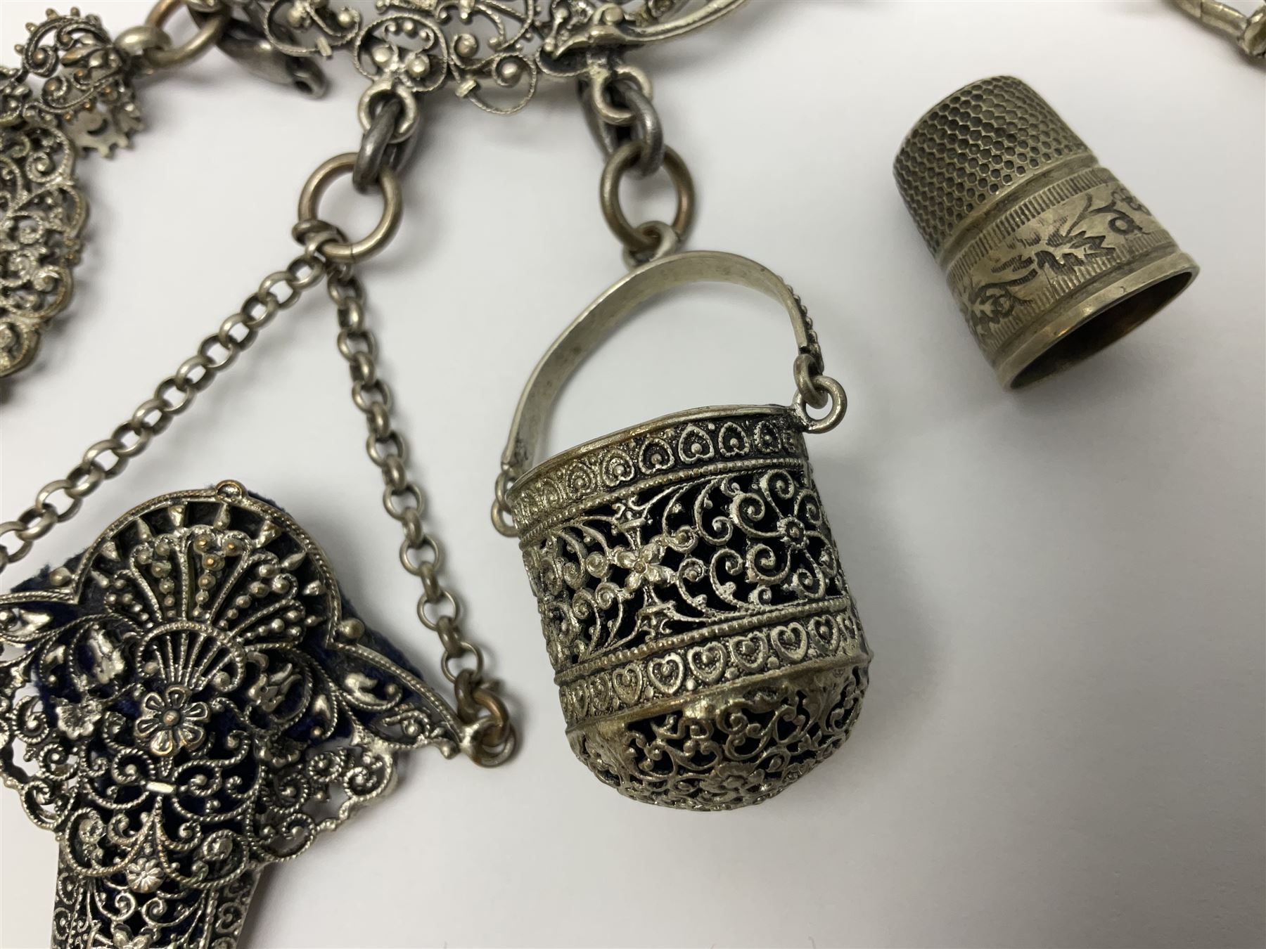 19th century continental silver plated chatelaine, the main body flanked with winged mythical beasts and central soldier slaying a dragon supporting three suspended items to include velvet lined small basket and long clasped filigree chain, together with a thimble