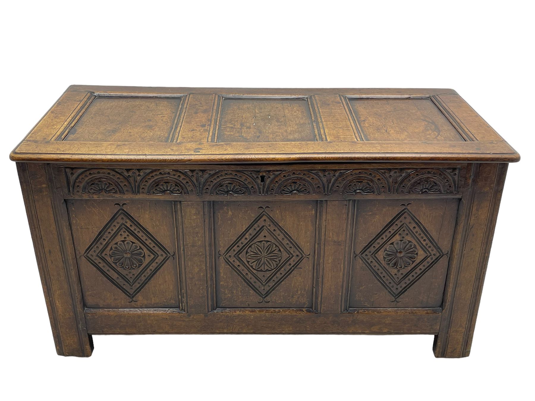 18th century oak coffer or chest, rectangular triple panelled hinged top with moulded edge enclosing main compartment and candle box, the frieze carved with repeating concentric lunettes and foliate patterns, the front fielded panels decorated with lozenges containing central flower heads, on stile supports