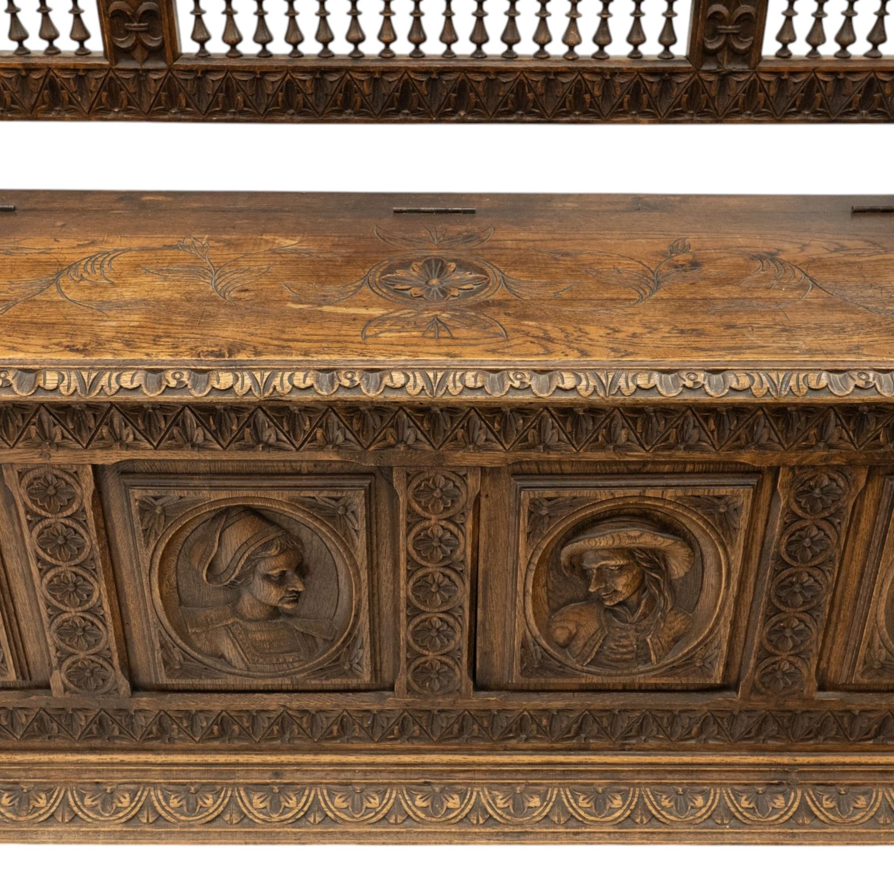 19th century European heavily carved oak hall settle, the impressive high-back with a pierced and carved acanthus pediment, over foliate and rosette carved back rails, flanking a central panel depicting a gentleman on horseback drinking, the hinged box seat over a quadruple panelled front with relief carved busts, lower moulded and carved edge on compressed bun feet