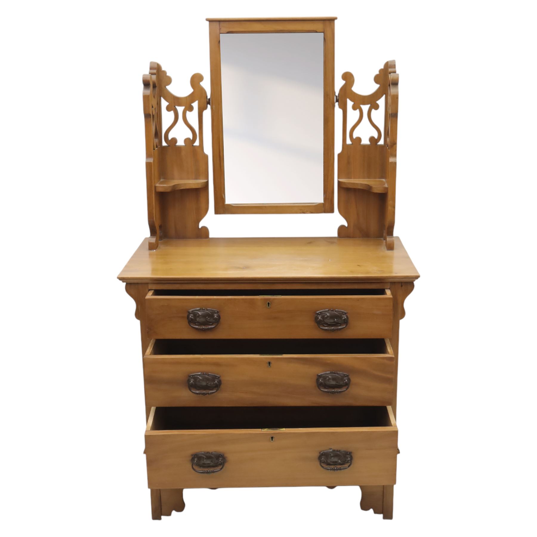 Edwardian stained pine dressing chest, the moulded top over three graduating drawers with pressed brass handles, shaped apron and bracket feet, the mirror back with rectangular plate on pivot supports, flanked by pierced Gothic style uprights with small corner shelves