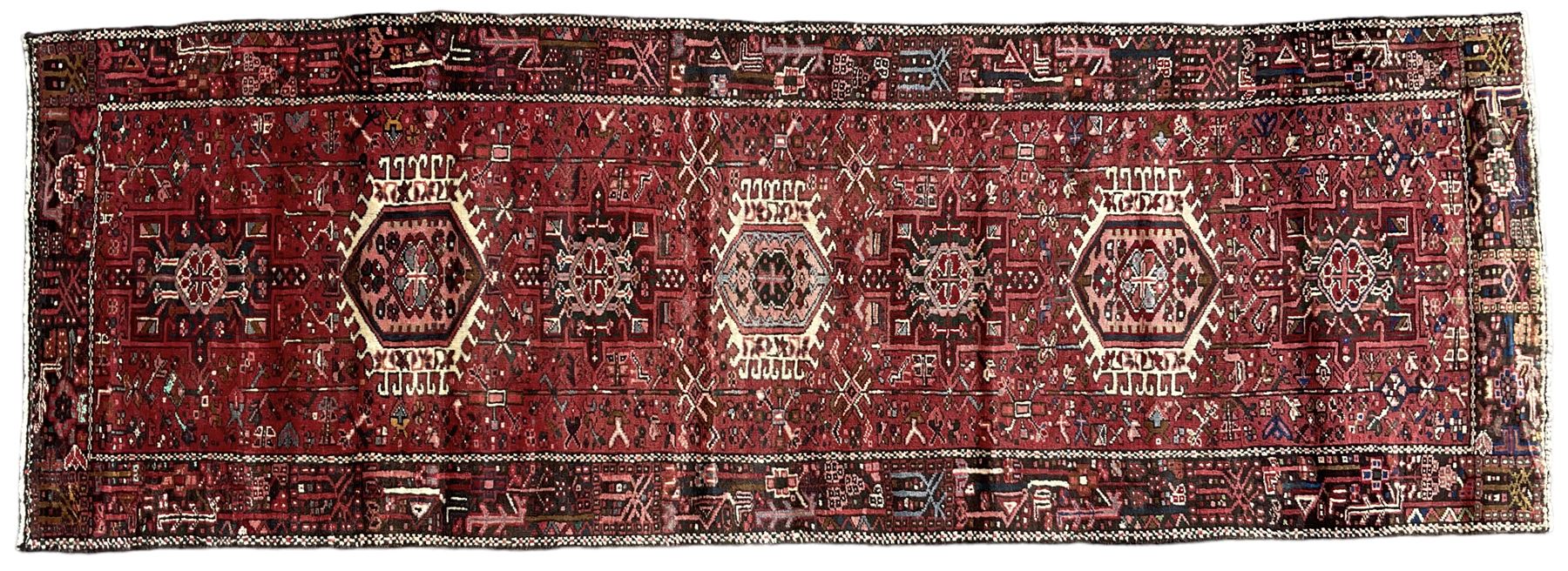 Persian Karajeh crimson ground runner rug, the field set with seven geometric lozenge medallions, the field decorated all over with stylised plant motifs, the banded border with repeating geometric shapes and patterns