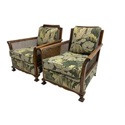 Early 20th century bergère lounge suite, mahogany framed with cane work back and sides, acanthus scroll carved uprights - three seat sofa (W167cm, H82cm, D83cm), and pair matching armchairs (W78cm), loose cushions upholstered in acanthus leaf scroll fabric with scatter cushions