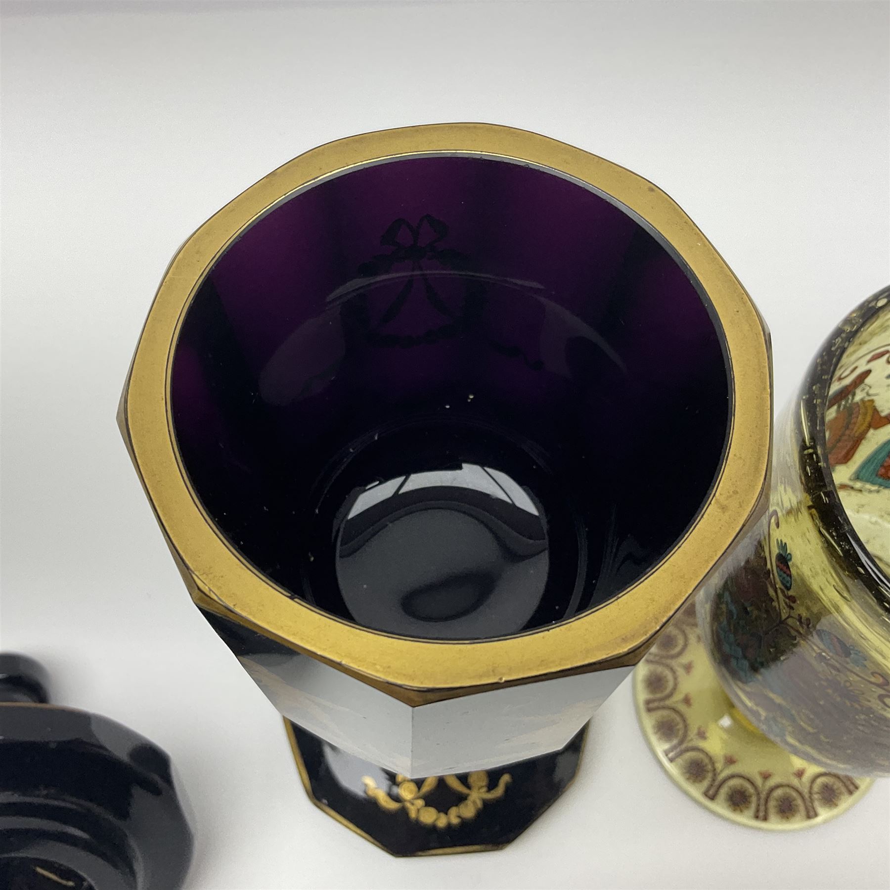 19th Century Bohemian amethyst glass lidded goblet, the bowl of faceted form, gilded with three children in period dress playing games, upon a knopped stem and conforming faceted foot, together with an art nouveau green glass goblet, with gilded rim, upon clear trumpet stem, and a hand blown wine glass, transfer printed with birds and three figures in period dress, tallest H29cm