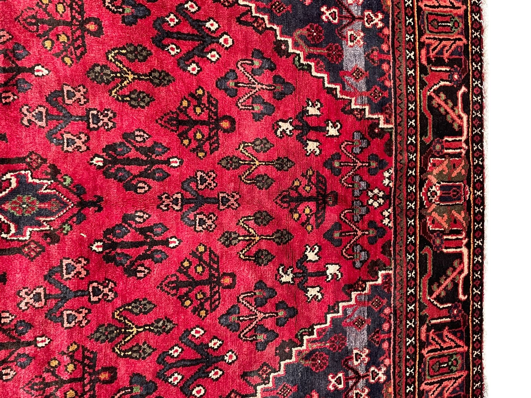 Persian Joshaghan crimson ground rug, stepped lozenge medallion surrounded by repeating foliate lozenge motifs, the border decorated with stylised plant motifs, within geometric guard stripes 