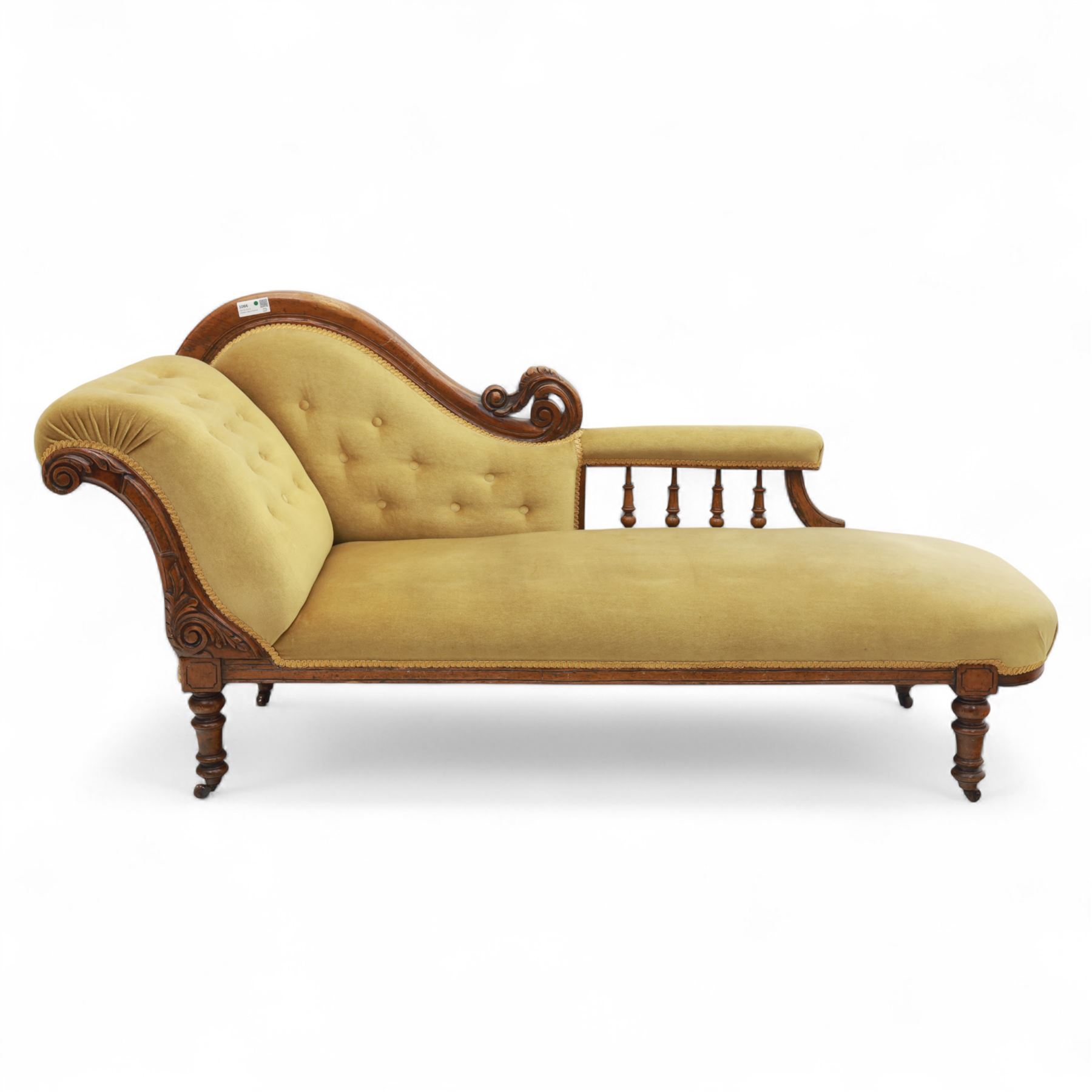 Victorian walnut chaise longue, carved with scrolling acanthus to the end supports and seat rail, upholstered in mustard coloured velvet, shaped and buttoned back and side with turned spindle gallery, raised on short turned legs with ceramic castors 