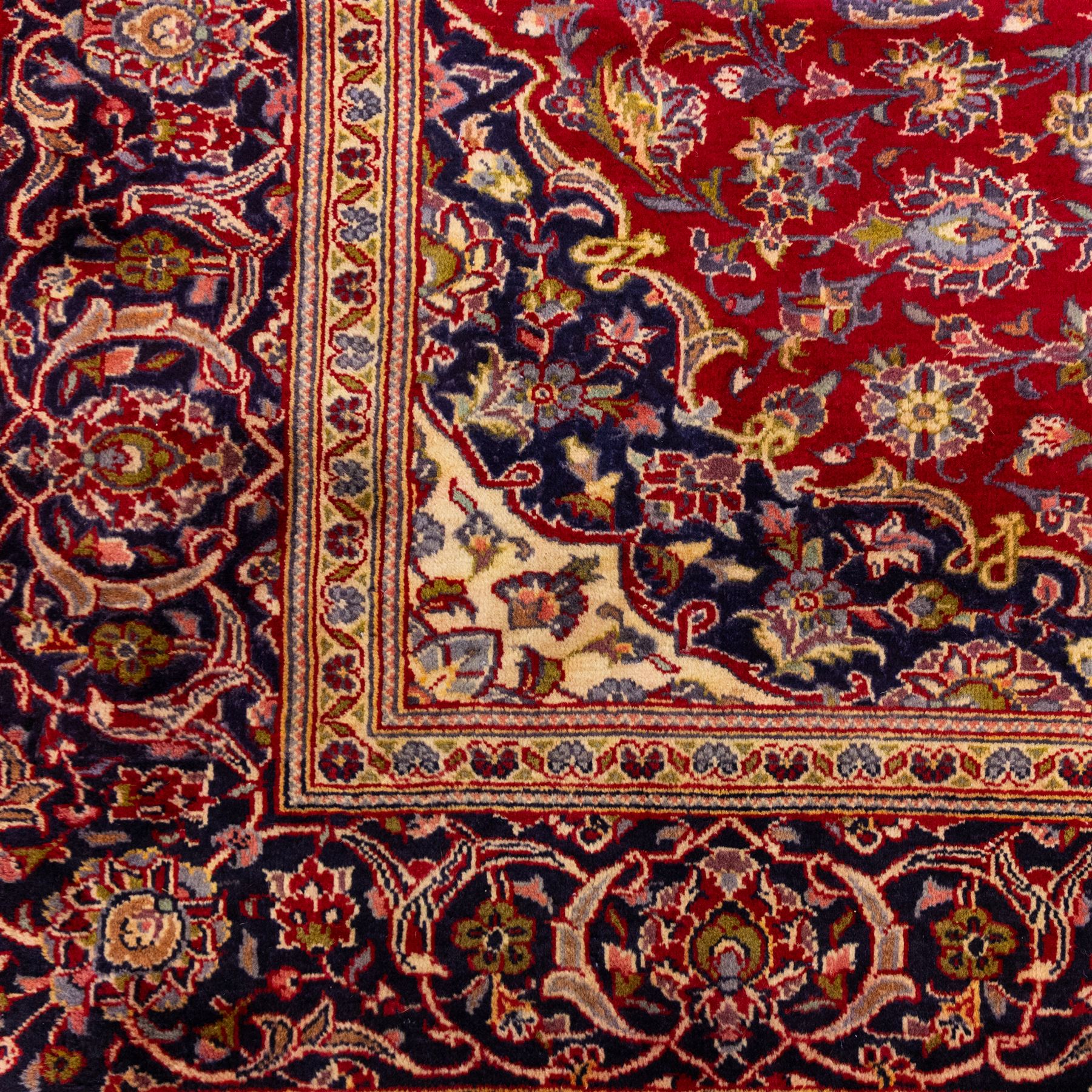Central Persian Kashan hand-knotted rug, crimson red field with central ivory and indigo floral medallion surrounded by an all-over arrangement of finely drawn palmettes, flowering vines, and rosettes, with corresponding navy blue spandrels enclosed by a floral main border with multiple guard stripes, with cotton fringe ends    