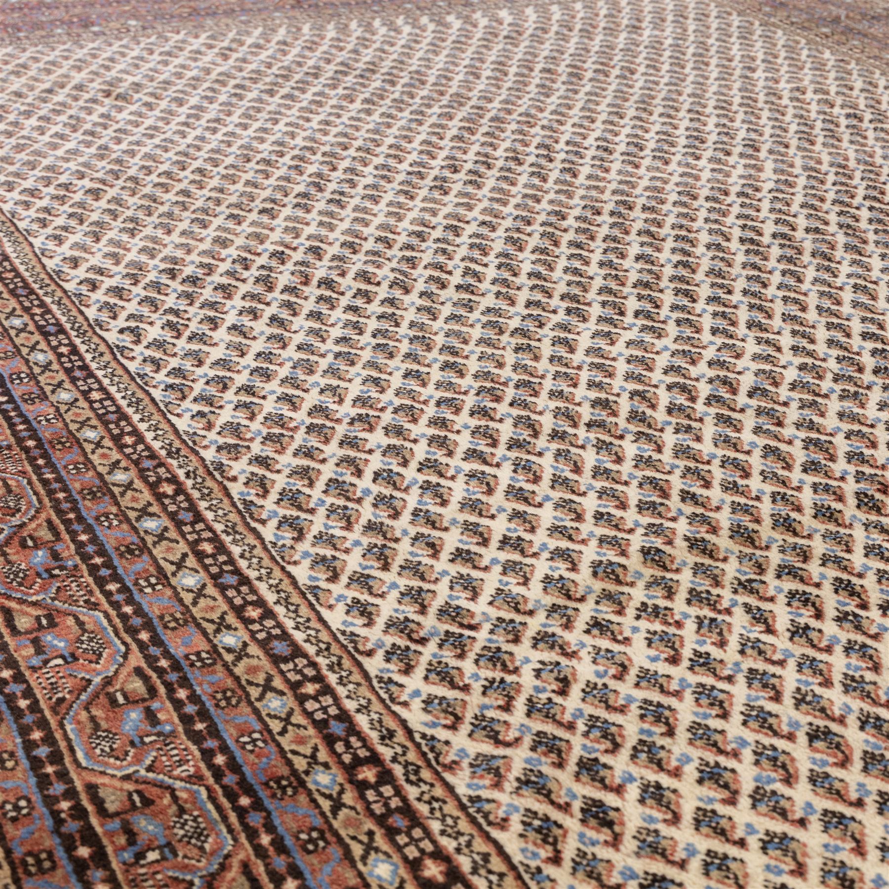 West Persian Botteh-Mir hand-knotted rug, ivory field decorated with an overall dense lattice design of small repeating boteh motifs in muted blue, rust, and brown tones, enclosed by a series of narrow borders incorporating stylized geometric and floral patterns with cotton fringe ends 