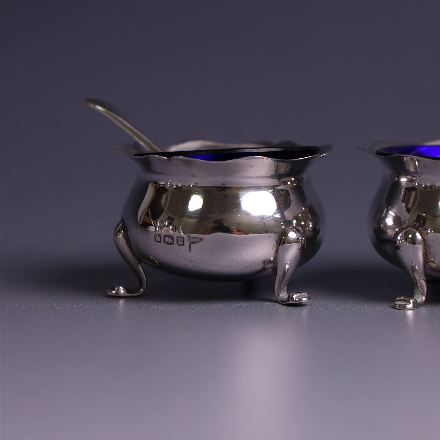 Early 20th Century four piece silver cruet set, comprising a pair of pepper shakers and a pair of open salts, each of circular form with shaped rims and upon three pad feet, hallmarked Walker & Hall, Sheffield 1912, the open salts with two silver plated salt spoons and blue glass liners 