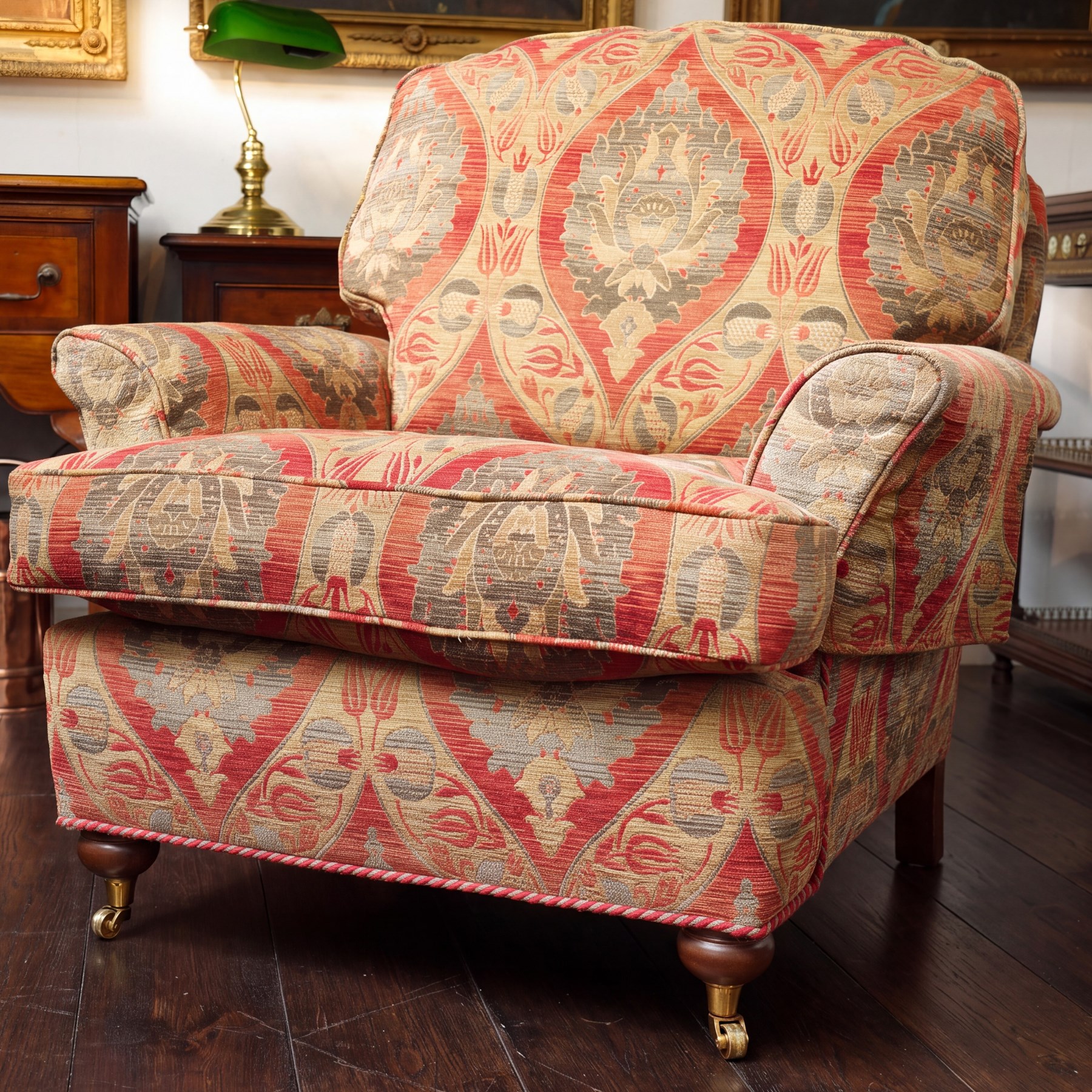 Duresta - traditional shape armchair with out-swept arms, upholstered in crimson ground fabric decorated with palmettes and foliate motifs with matching loose and scatter cushions, raised on compressed bun feet with brass cups and castors