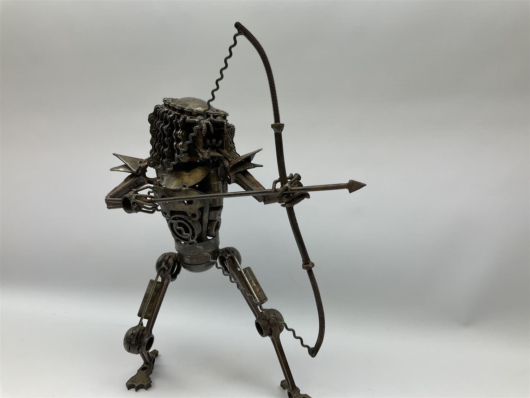 Predator metal sculpture, made with scrap metal, with articulated body, bike chain hair, and bow and arrow, H45cm