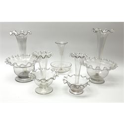 Four Victorian clear glass epergnes, with single frilled trumpet above a frilled bowl and circular foot, largest example H24cm, smallest example H15.5cm, together with a further Victorian clear glass epergne with etched foliate decoration to trumpet and bowl. 