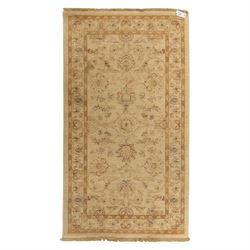 Cream ground wool rug, with faded floral medallion and scrolling foliate design, enclosed ...