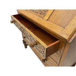 Early 20th century golden oak bureau, panelled fall front carved with scrolling foliage enclosing fitted interior, above three long drawers, the top drawer front with blind fretwork decoration
