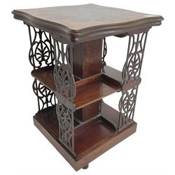 Edwardian mahogany revolving bookcase, the shaped moulded top inlaid with cusped panel and trailing bellflowers within a satinwood frame, foliate pierced upright splats and central square column supporting two tiers, on cruciform base with brass and ceramic castors 