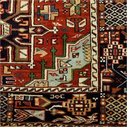 North West Persian Karajeh hand-knotted rug, terracotta ground, with a stepped geometric pole medallion design in blue, ivory and dark navy tones, surrounded by angular tribal motifs incorporating stylised flowerheads, hooked devices and geometric vine work, enclosed by a dark navy border with repeating rosettes and angular leaf motifs, flanked by narrow patterned guard stripes, with cotton fringes