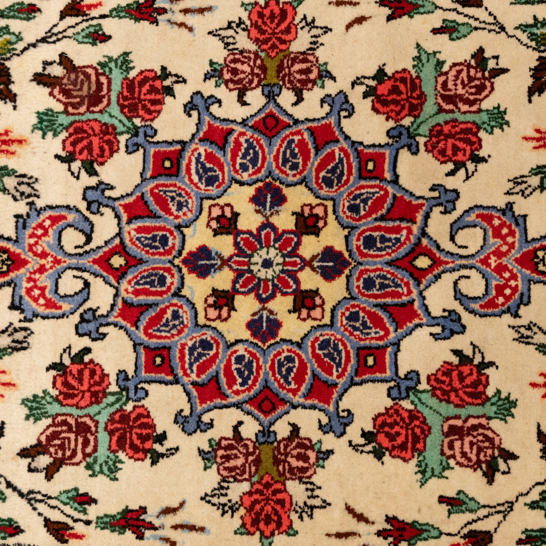 Two small rugs, an ivory ground example decorated with a central floral medallion and scattered rose sprays, enclosed by a navy foliate border (62cm x 101cm), and a crimson pictorial mat worked with seated figures, an animal and birds amongst flowering plants (45cm x 79cm) (2)