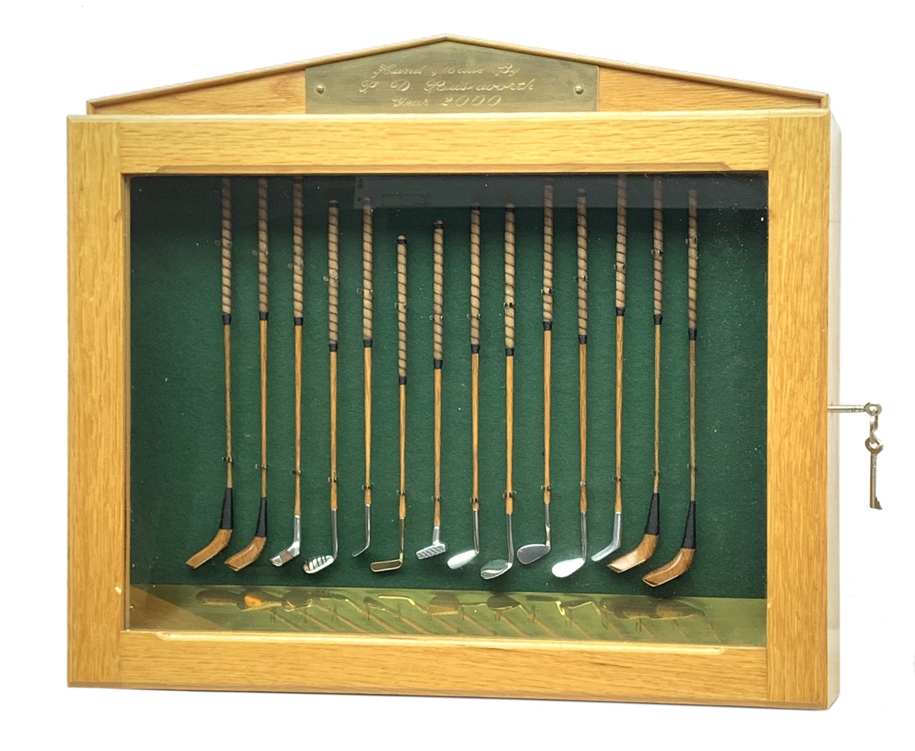 Modern handcrafted miniature set of fourteen 19th century style golf clubs by P.D. Rushworth dated 2000, each with turned wooden shaft and leather grip, comprising four woods including long nose driver, brassie and hooked face, and ten other metal head clubs including jigger, water iron, rut iron, anti-shank iron, wryneck iron, mammoth iron, Schenectady putter, etc., displayed in a baise lined architectural style oak case with hinged door, annotated brass strip and maker's plaque, longest club 28cm, case W52cm, H44cm