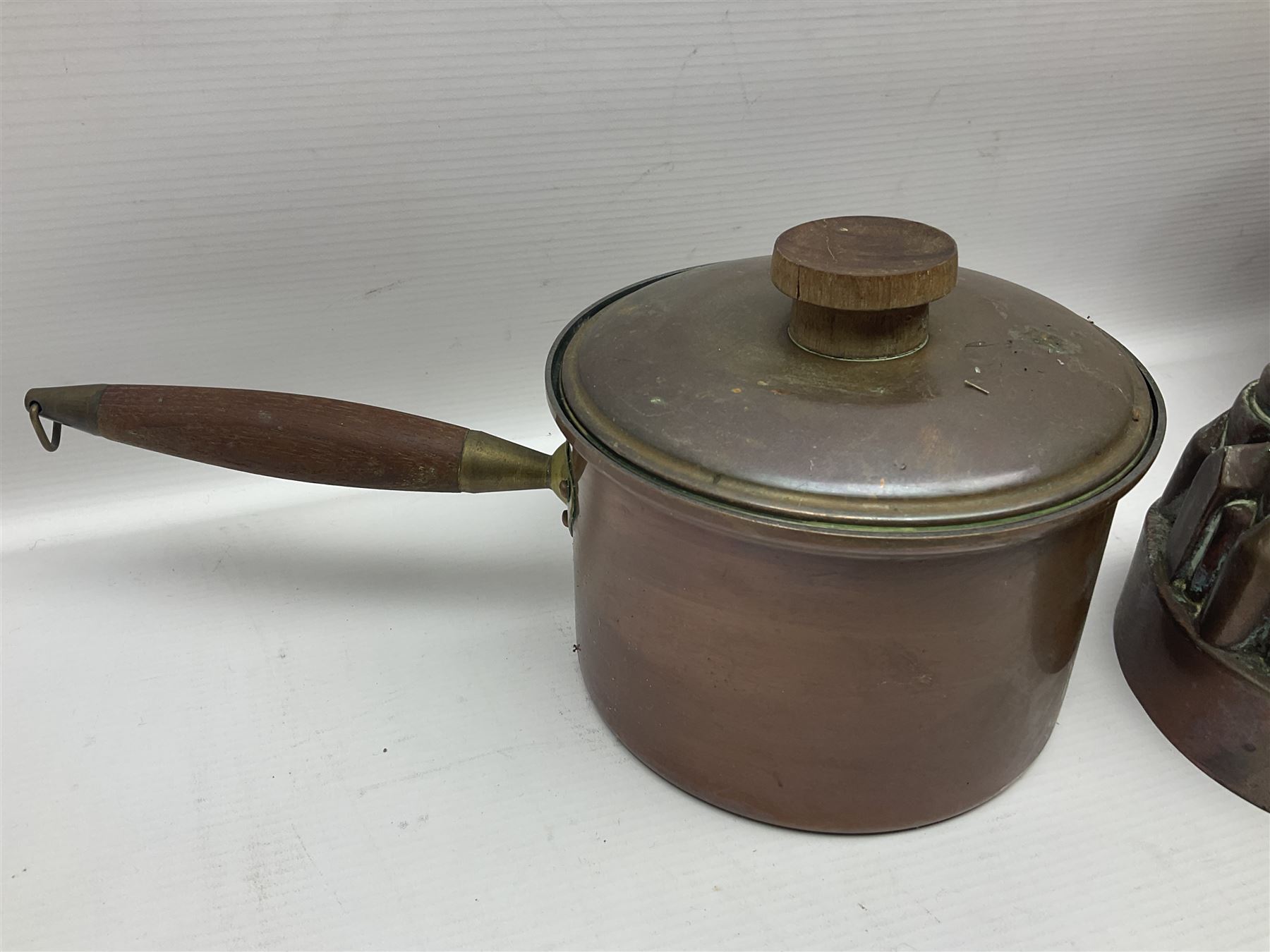 Four Victorian copper moulds, together with a graduating set of copper pans with wooden handles and finials to covers, largest pan 