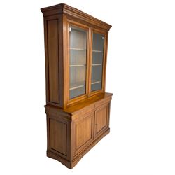 French cherry wood bookcase on cupboard, projecting cornice over two cupboard doors with bevelled glass panels enclosing three adjustable shelves, base fitted with two cushion drawers over double cupboard