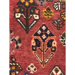 Persian Qashqai crimson ground runner, the field decorated with repeating diamond-shaped medallions flanked by angular floral motifs, the spandrels with intricate boteh designs, framed by an ivory border with stylised floral patterns and scrolling vines
