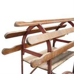 Cast iron and wooden saddle rack, arch form with shelf beneath and wheels to one end, pair of shaped handle poles