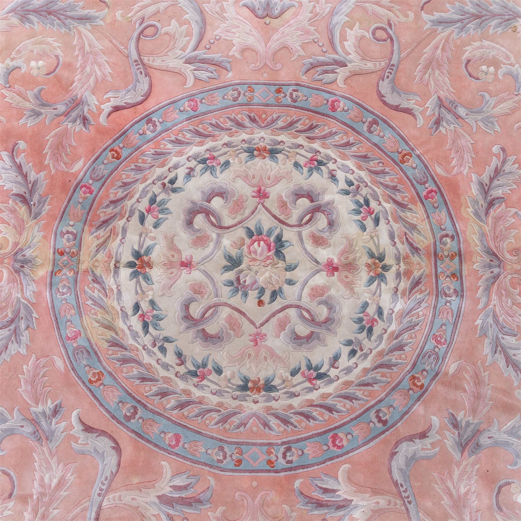 Large late 20th century Aubusson style wool carpet, peach and pastel toned field with central floral medallion enclosing scrolling acanthus and and foliate sprays, surrounding field decorated with further stylized foliage and and floral ornament, within shaped reserves and indigo corner spandrels, enclosed by narrow guard border, cotton fringe ends