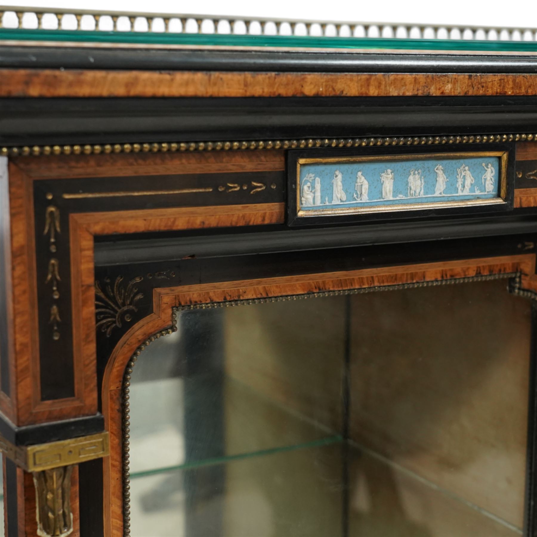 Victorian amboyna and ebonised credenza with glass top, the freeze fitted with two Wedgewood plaques and brass beading above crossbanded arched glazed mirror door flanked by two glazed cabinet doors with two removable glass shelves between four gilt brass reeded floral columns, supported on bun style feet