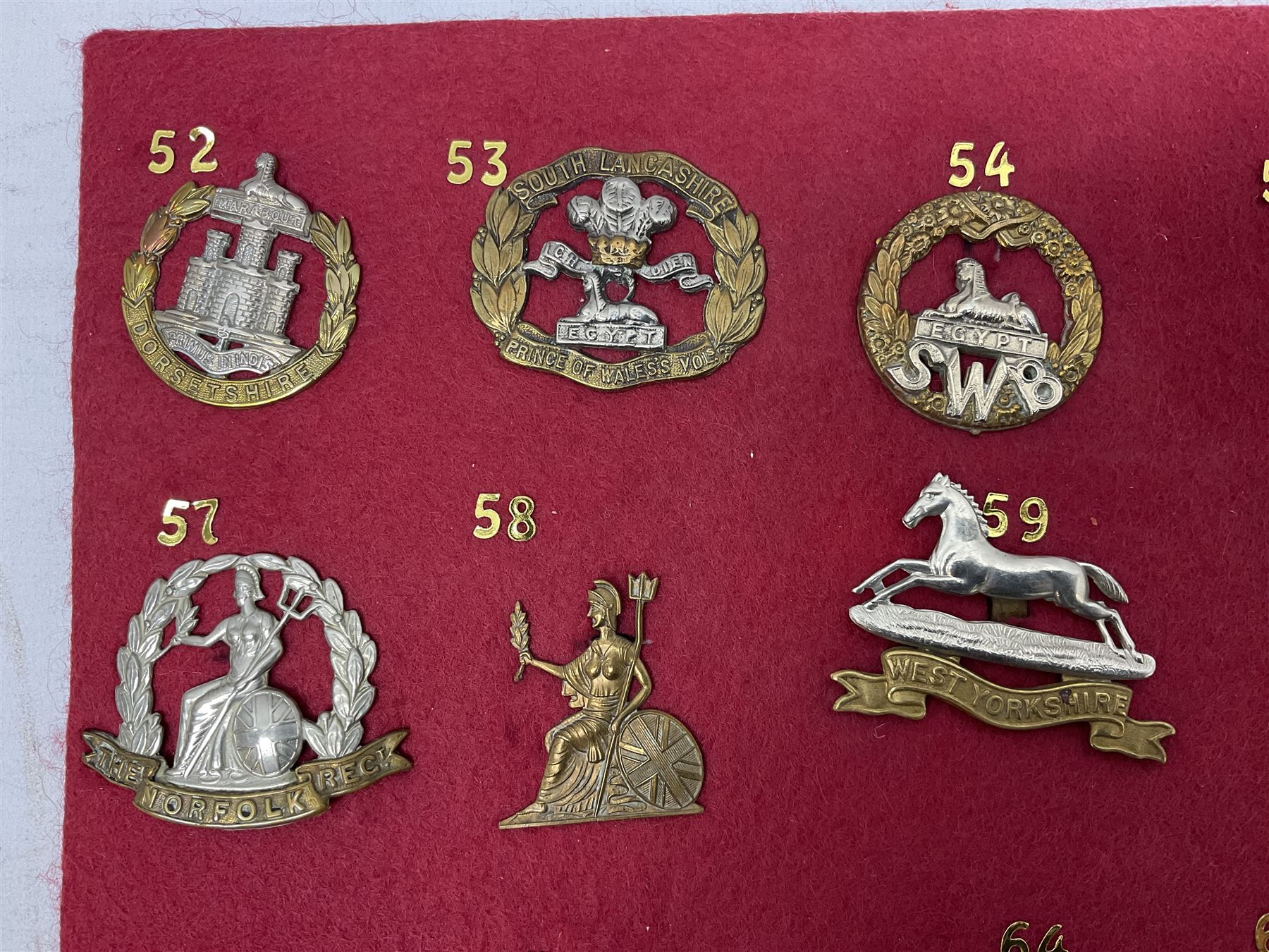 Twenty cap badges including Welsh Guards, Kings Royal Irish Hussars, York & Lancaster,  Loyal Suffolk Hussars, North Stafford, Durham Light Infantry, Cheshire, West Yorkshire, Norfolk, South Wales Borderers, Dorsetshire etc; mounted on a board for display