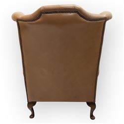 Contemporary set of two tan leather armchairs, comprising a deep-buttoned chesterfield and a matching wingback chair, both with rolled arms, studded borders