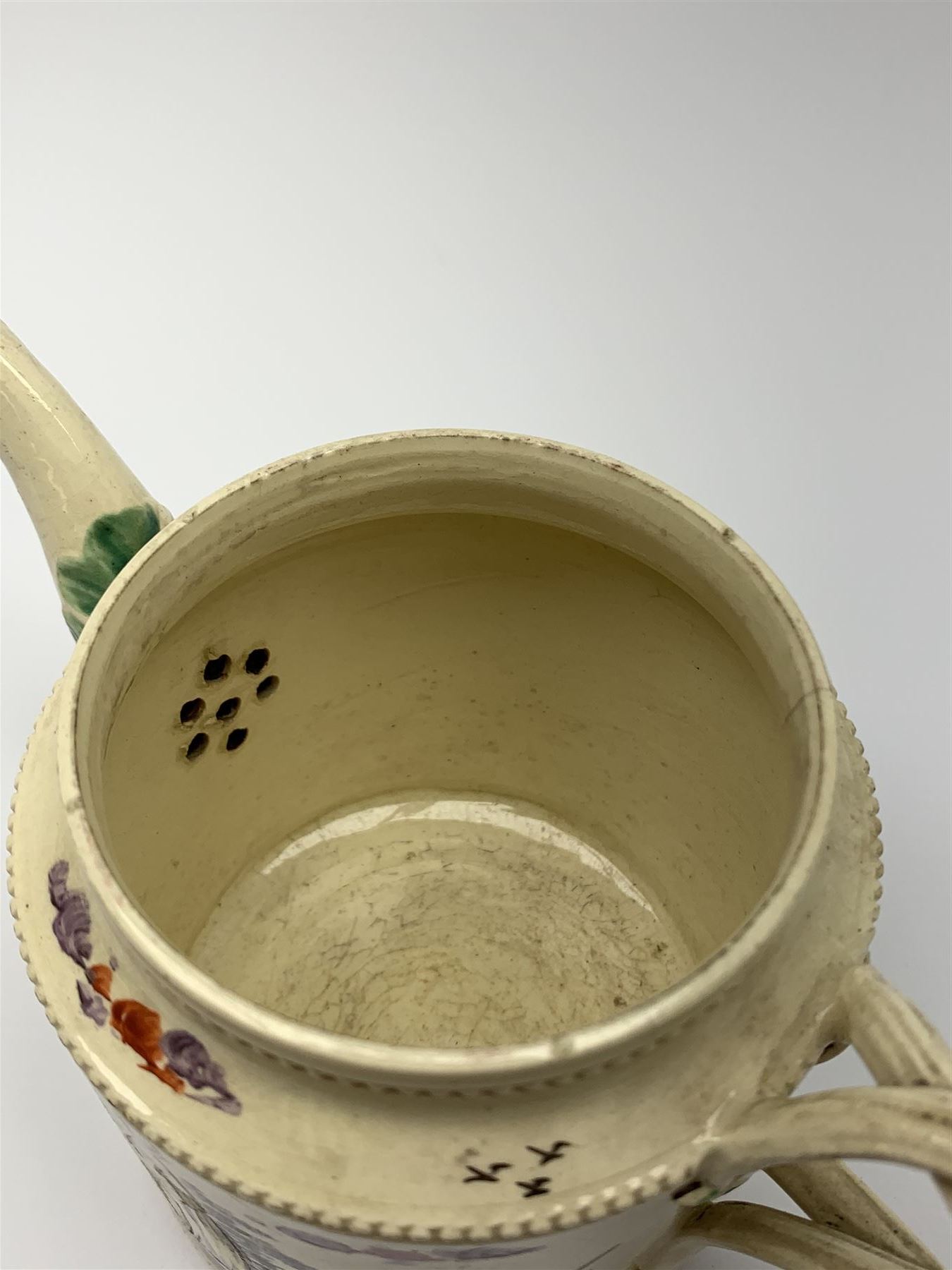 18th century creamware teapot, probably Leeds, with reeded entwined handle and floral finial to the cover, the body with hand painted polychrome decoration of figure to one side, and floral spray to the other, collectors paper label beneath inscribed Leeds Pottery, H11.5cm