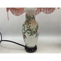 Four Oriental ceramic table lamps, to include example modelled as a ginger jar decorated with birds, figures and flowers, another example of tapering form decorated with a river and pagoda landscape scene, and pair of smaller lamps decorated with blossoming branches, all with pink tasselled fabric shades and upon circular hardwood bases, largest H38cm excl fitting