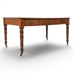 Victorian pitch pine writing table with leather inset top, rectangular top with three frieze drawers, pierced brass handles, raised on turned and fluted supports terminating in castors