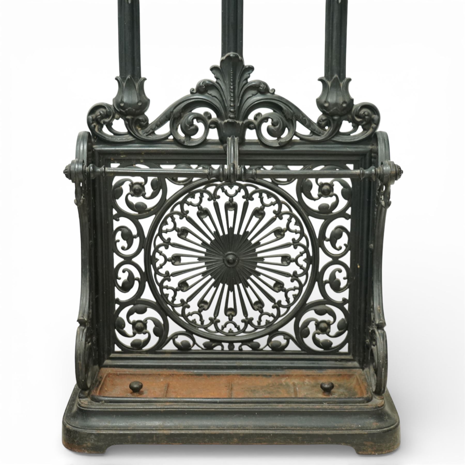 Late 19th century cast iron stick stand, the arched back with scrolling foliate decoration, fitted with multiple hooks, the lower section with pierced panels centred by a radiating sunburst motif, raised on a rectangular drip tray base