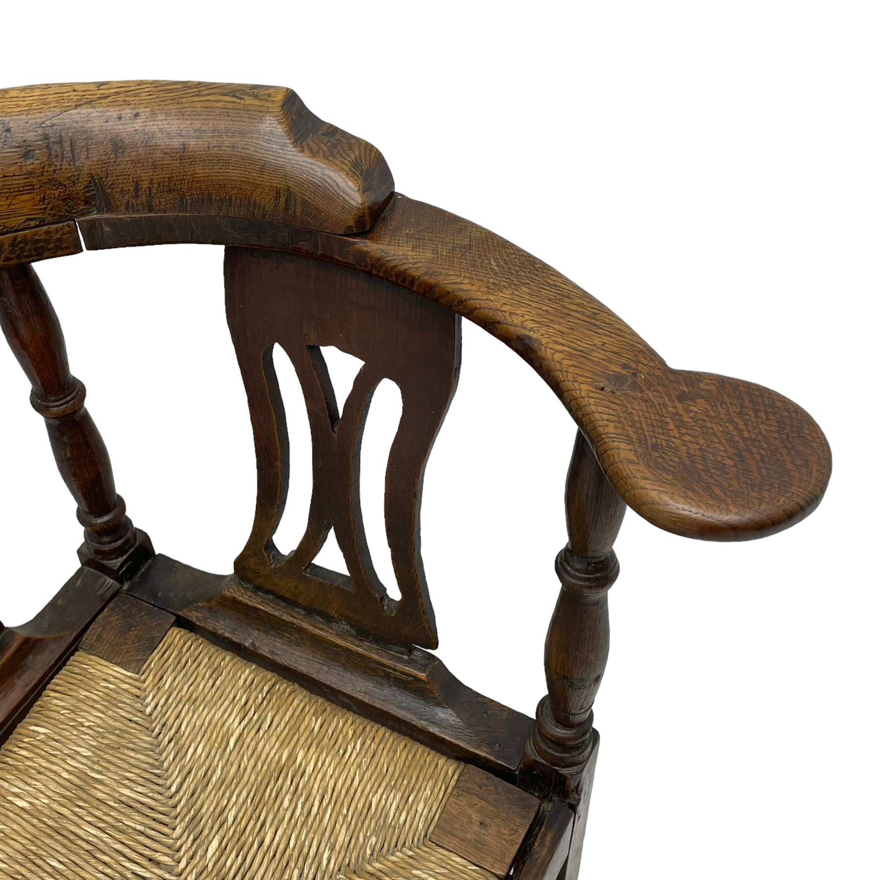 18th century country elm and oak corner chair, the shaped cresting rail terminating to swept arm resets, supported by turned columns and pierced shaped splats, over a drop-in rush seat, raised on square supports united by box stretcher
