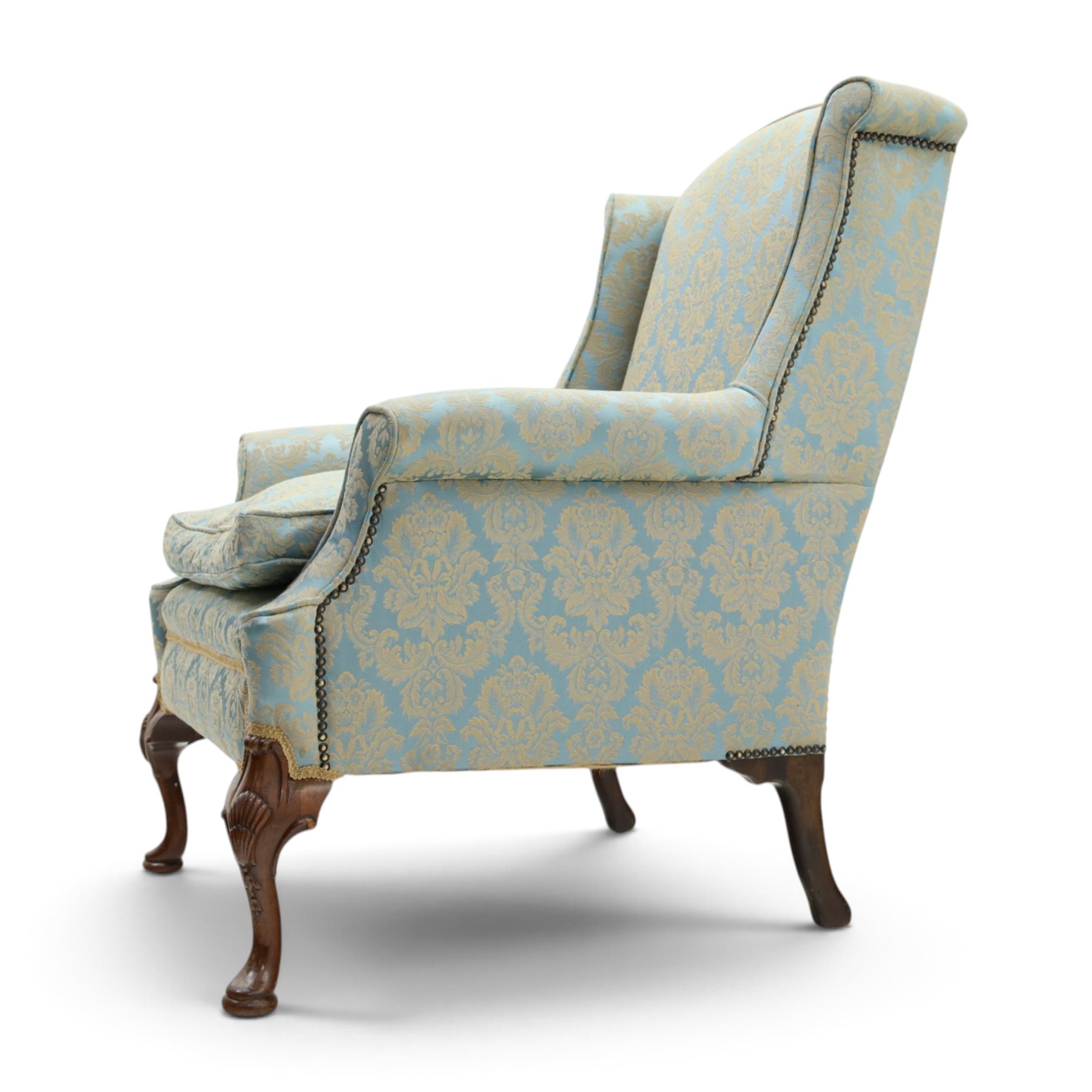 Georgian design carved mahogany framed wingback armchair, high wingback over sprung seat and loose cushion with rolled arms, upholstered in cyan ground gilt foliate damask fabric, on shell-carved cabriole supports with pad feet