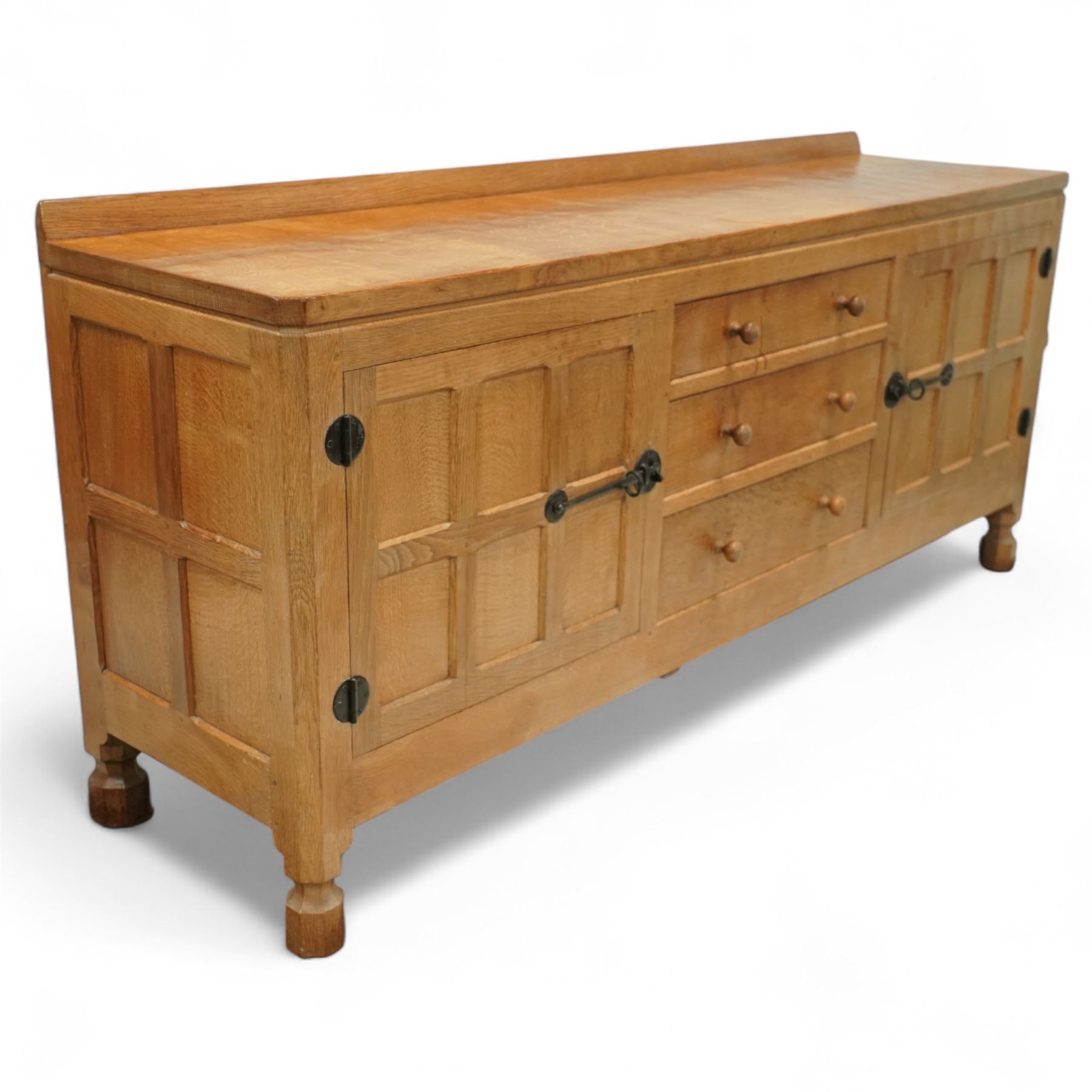 Mouseman - oak sideboard rectangular adzed top with raised back over three central drawers and two flanking cupboards, enclosed by panelled doors with wrought metal fixtures, the canted upright carved with mouse signature, on octagonal feet, by the workshop of Robert Thompson, Kilburn