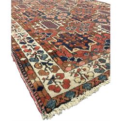 Persian crimson ground rug, the field decorated with three rows of stylised plant medallions and small flowerhead motifs, repeating floral design border with guards 