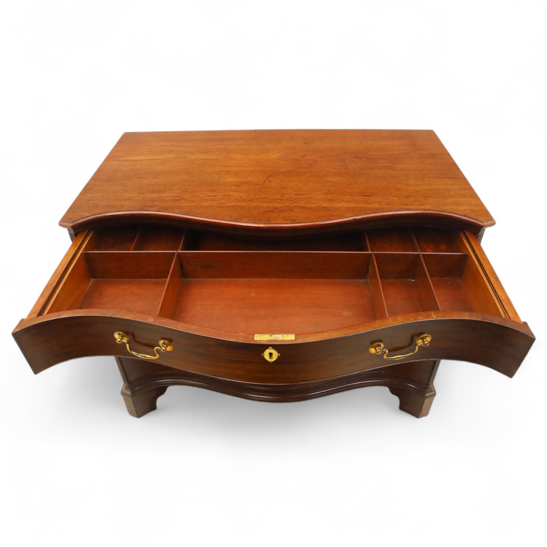 George III mahogany serpentine chest, moulded top over four cock-beaded drawers, the top drawer fitted with baize lined slide opening to reveal divisions,  enclosed by canted and fluted upright corners, the drawer fronts fitted with brass swan neck handles and circular plates with oval escutcheons, lower moulded edge over bracket feet, on lignum vitae castors