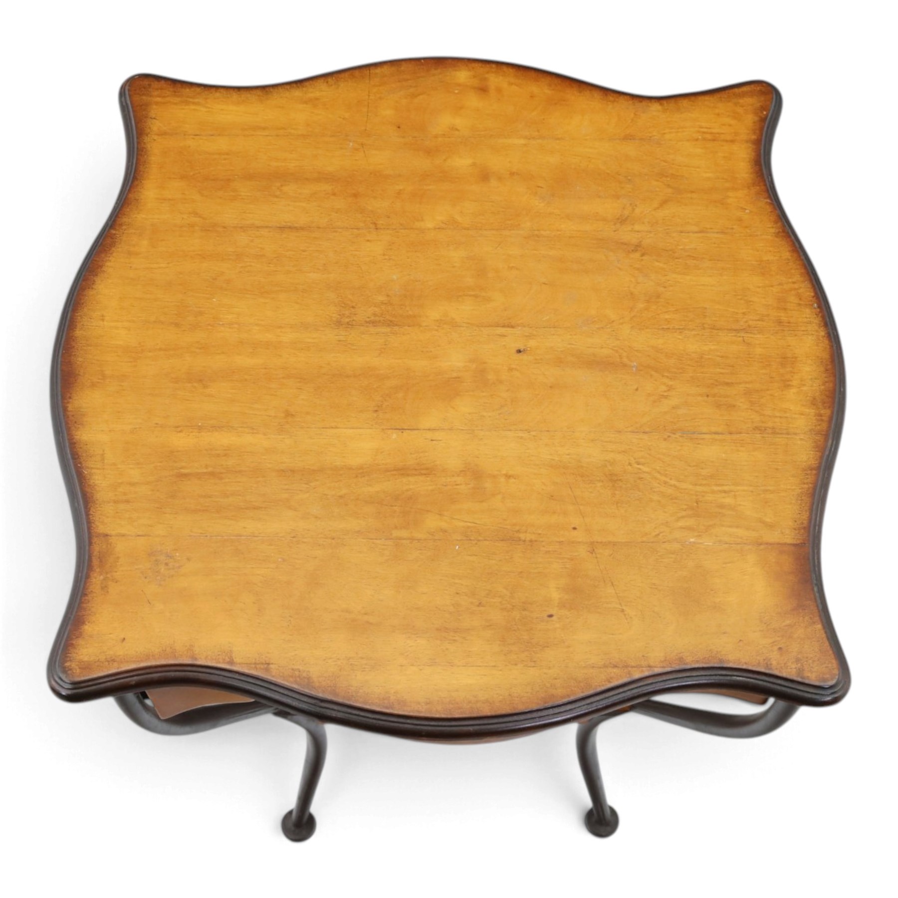 Art Nouveau style occasional table, serpentine shaped top with dark moulded edge, shaped apron and lower shelf, raised on four curved metal supports