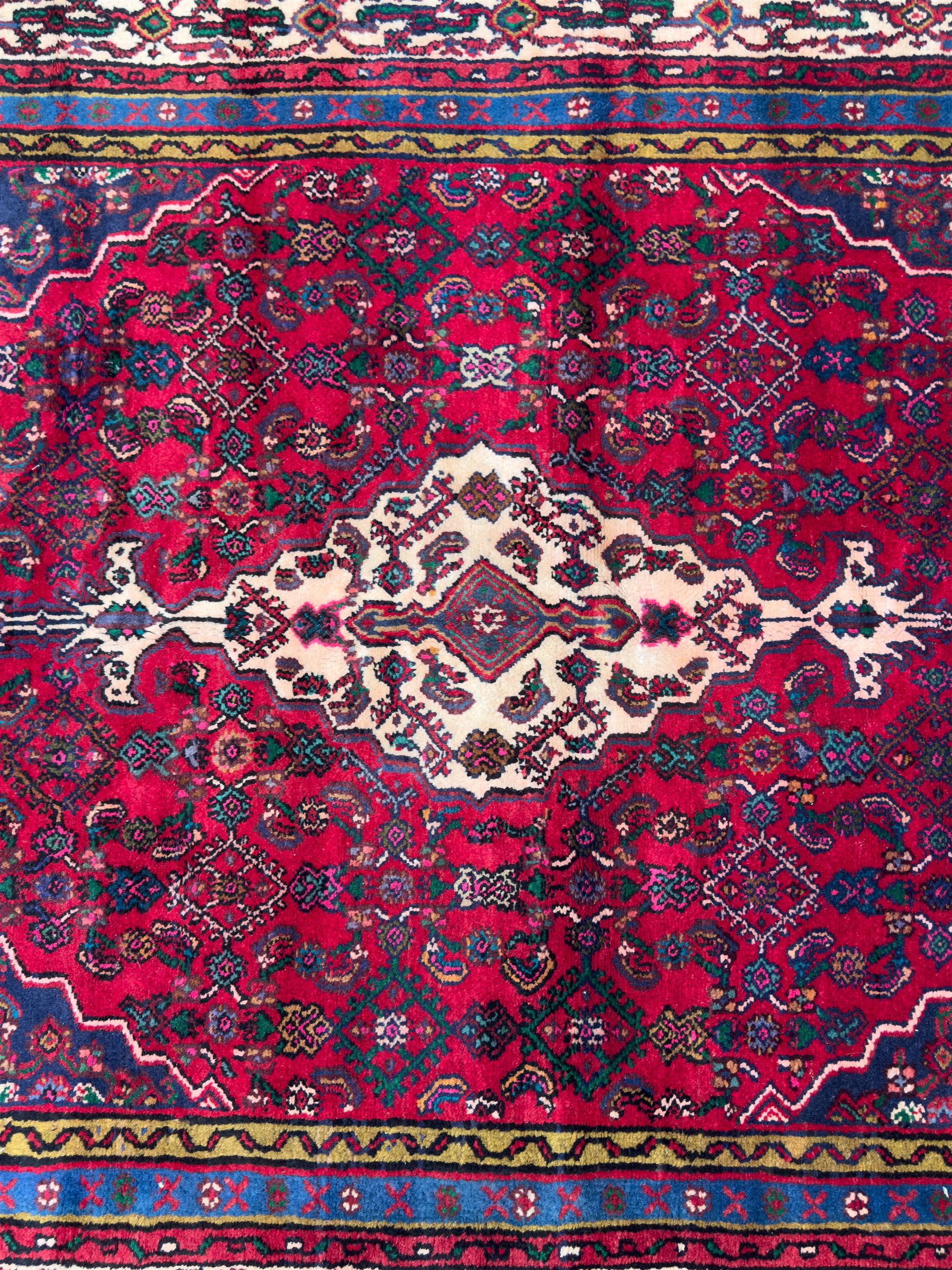 Northwestern Persian Hamadan hand-knotted rug, madder red field with a lozenge medallion enclosing an ivory centrepiece, indigo spandrels within an ivory border of stylized floral motifs between multiple guard borders 