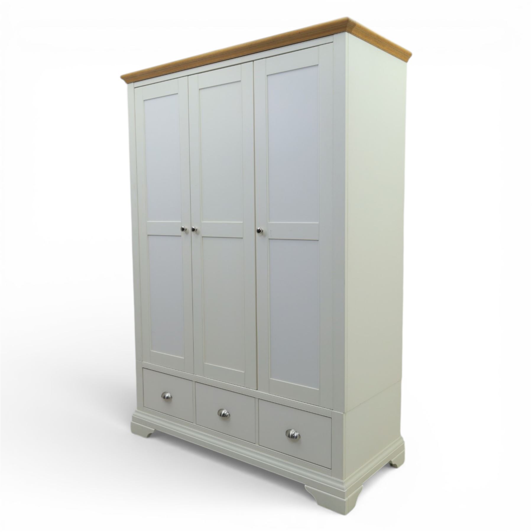 Modern triple wardrobe in white finish with oak moulded top enclosed by three doors with three drawers to base, with metal cup handles raised on bracket feet