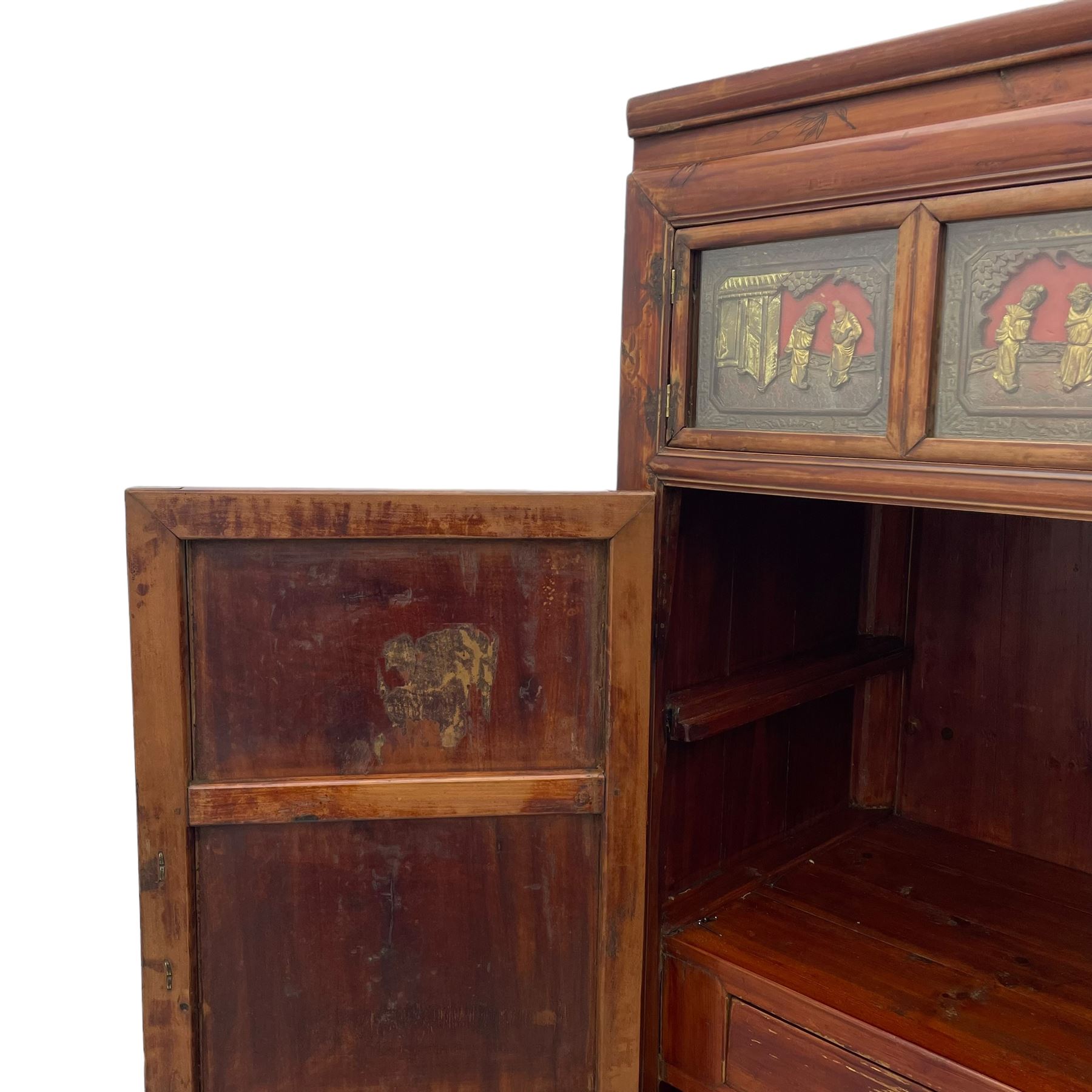 Late 19th century Chinese Qing dynasty red and black lacquered wood cabinet,  Fujianese province, upper cupboard enclosed by two doors with relief carved and gilt panels depicting figures behind glass, the large cupboard enclosed by two panelled doors carved with trailing foliate branches and birds, inscribed with Chinese characters, to the left ‘The red mountains are in the shape of Phoenixes and appear auspicious’ and to the right, ‘Wealth and honour are given by flowers and I hear the sound of the phoenix', fitted with two drawers, on square supports with carved brackets 